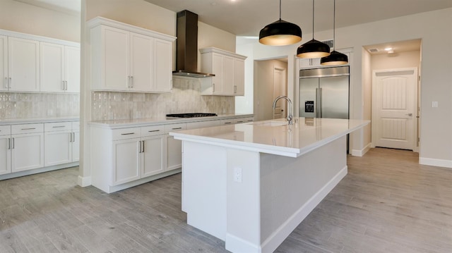951 Talus Way S, Madera, CA 93636 - kitchen featuring wall chimney exhaust hood, built in refrigerator, light wood-type flooring, an island with sink, and backsplash