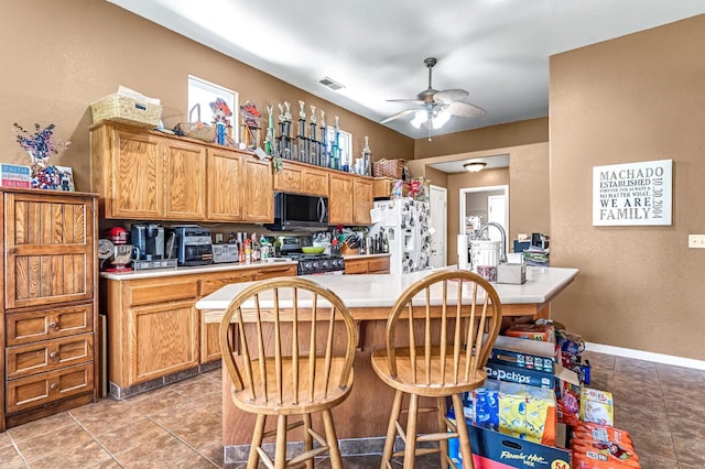 3742 Via Capitola, Madera, CA 93637 - kitchen featuring white fridge with ice dispenser, stainless steel range with gas cooktop, light countertops, ceiling fan, and a kitchen bar
