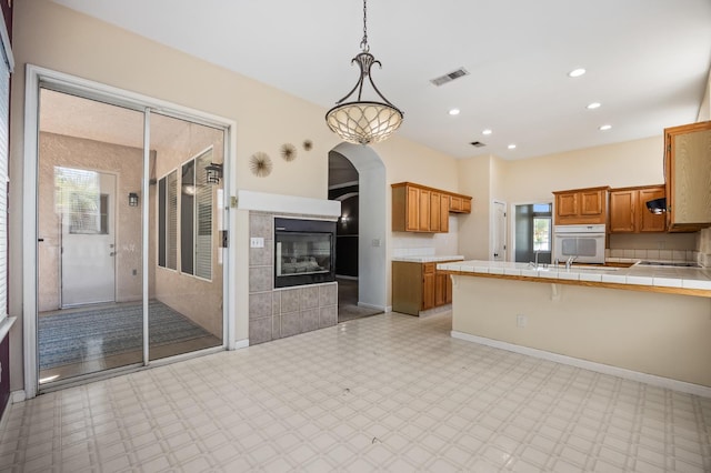 7507 N Constance Ave, Fresno, CA 93722 - kitchen with tile counters, brown cabinetry, white oven, a peninsula, and light floors