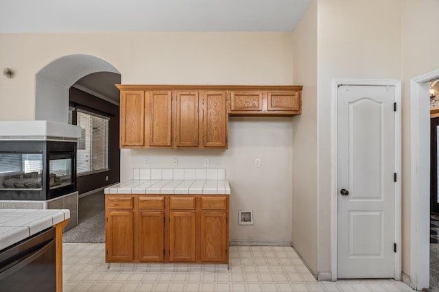 7507 N Constance Ave, Fresno, CA 93722 - kitchen with tile countertops, light flooring, arched walkways, stainless steel dishwasher, and brown cabinetry