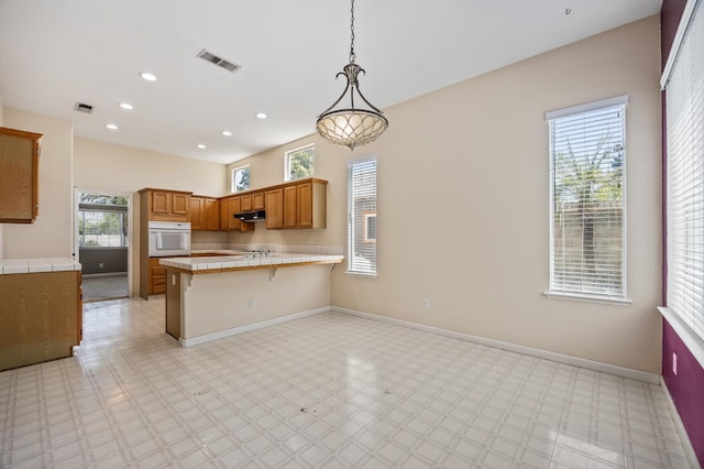 7507 N Constance Ave, Fresno, CA 93722 - kitchen with white oven, a peninsula, tile countertops, under cabinet range hood, and light floors