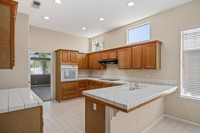 7507 N Constance Ave, Fresno, CA 93722 - kitchen featuring white oven, light floors, under cabinet range hood, black electric stovetop, and brown cabinetry
