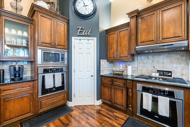 2639 Maine Ave, Clovis, CA 93619 - kitchen featuring appliances with stainless steel finishes, under cabinet range hood, decorative backsplash, dark wood finished floors, and glass insert cabinets