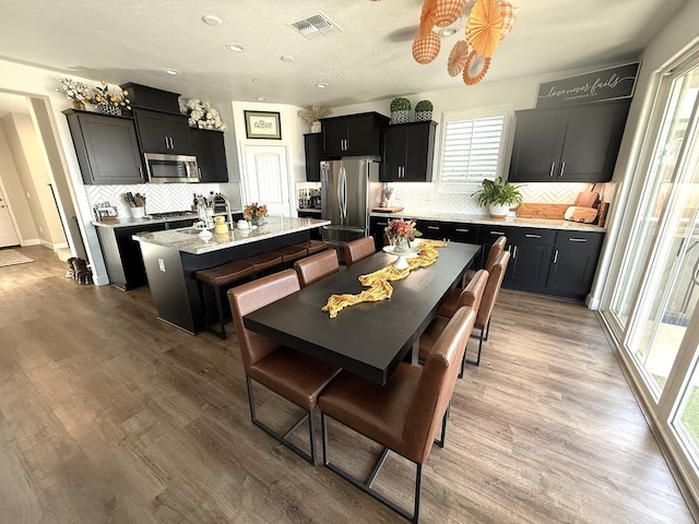 971 Dana Rd W, Madera, CA 93636 - kitchen with appliances with stainless steel finishes, an island with sink, dark cabinets, decorative backsplash, and wood finished floors