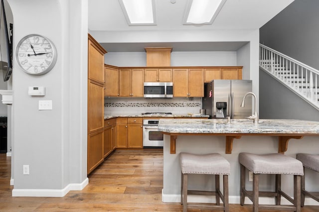 5313 W King Fisher Ln, Fresno, CA 93722 - kitchen with appliances with stainless steel finishes, light wood finished floors, a breakfast bar area, decorative backsplash, and light stone counters