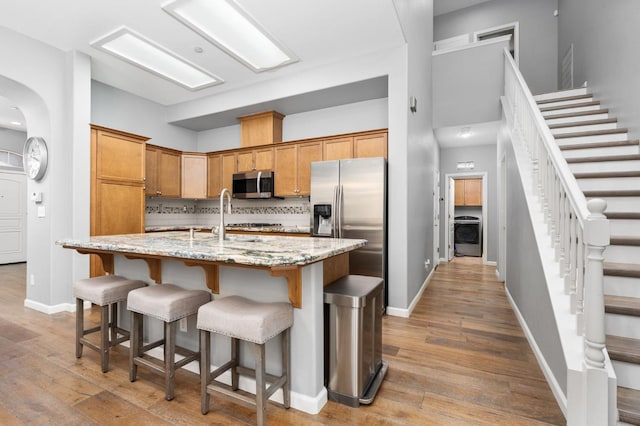 5313 W King Fisher Ln, Fresno, CA 93722 - kitchen featuring appliances with stainless steel finishes, hardwood / wood-style floors, light stone countertops, a kitchen island with sink, and decorative backsplash