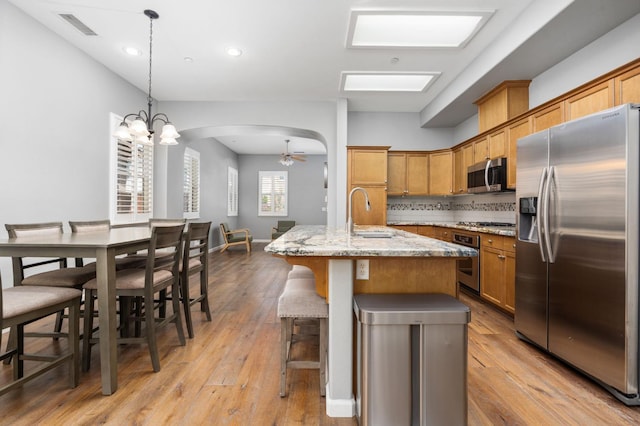 5313 W King Fisher Ln, Fresno, CA 93722 - kitchen with stainless steel appliances, arched walkways, light stone countertops, a kitchen breakfast bar, and light wood-type flooring