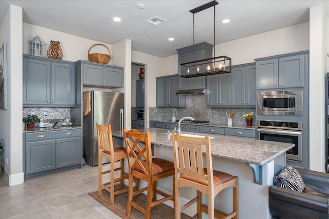 602 Pinnacle Dr W, Madera, CA 93636 - kitchen with appliances with stainless steel finishes, light stone countertops, decorative backsplash, a kitchen bar, and recessed lighting