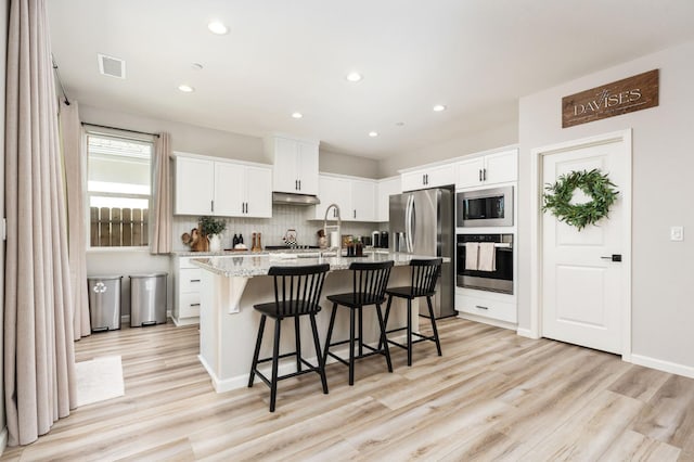 1275 Traverse Dr S, Madera, CA 93636 - kitchen with appliances with stainless steel finishes, light wood-type flooring, a kitchen breakfast bar, white cabinets, and a kitchen island with sink