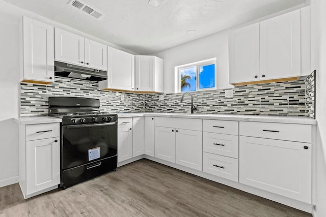 124 E 4th St, Hanford, CA 93230 - kitchen featuring black gas range oven, under cabinet range hood, light countertops, light wood-type flooring, and a textured ceiling