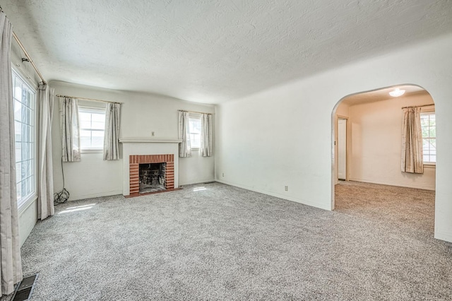 4740 E Washington Ave, Fresno, CA 93702 - unfurnished living room featuring a textured ceiling, arched walkways, a brick fireplace, and carpet