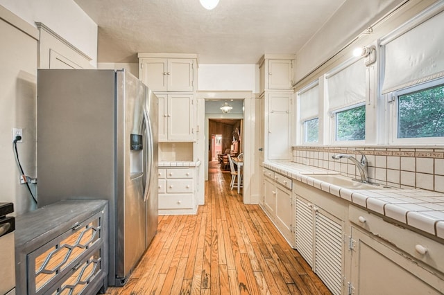 3303 E Mono Ave, Fresno, CA 93702 - kitchen with stainless steel fridge, white cabinetry, light wood-type flooring, backsplash, and tile countertops