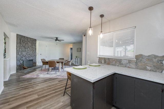 4245 N Manila Ave, Fresno, CA 93727 - kitchen featuring ceiling fan, light wood finished floors, a stone fireplace, hanging light fixtures, and dark cabinets