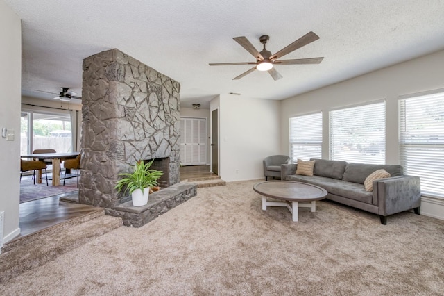 4245 N Manila Ave, Fresno, CA 93727 - living room featuring ceiling fan, a stone fireplace, a textured ceiling, and carpet floors