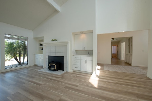 1535 S Homsy Ave, Fresno, CA 93727 - unfurnished living room featuring high vaulted ceiling, a wood stove, light wood-style flooring, and beam ceiling