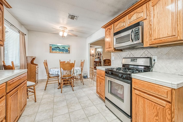 5400 Amber Ave, Clovis, CA 93619 - kitchen featuring appliances with stainless steel finishes, decorative backsplash, a ceiling fan, tile counters, and light tile patterned flooring