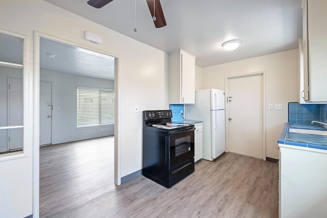 2044 Mayfair Dr W, Fresno, CA 93703 - kitchen with black / electric stove, light wood-style floors, freestanding refrigerator, tasteful backsplash, and white cabinetry