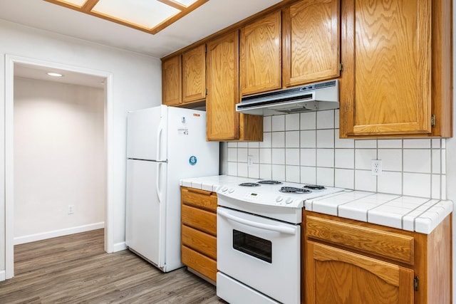 5137 W Stuart Ave, Fresno, CA 93722 - kitchen with white appliances, under cabinet range hood, backsplash, light wood-style floors, and tile countertops