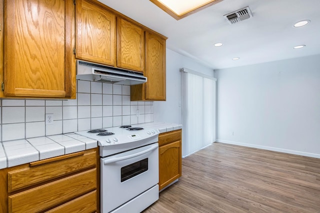5137 W Stuart Ave, Fresno, CA 93722 - kitchen featuring under cabinet range hood, white electric stove, backsplash, brown cabinets, and light wood finished floors
