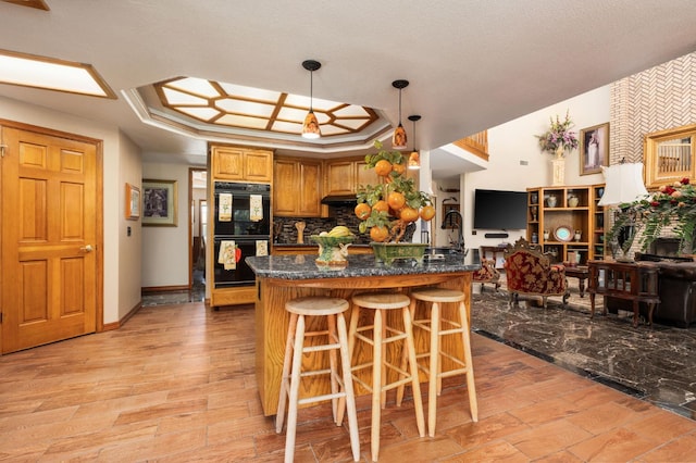 7207 E Bremer Ave, Fresno, CA 93737 - kitchen featuring a breakfast bar area, tasteful backsplash, under cabinet range hood, brown cabinets, and pendant lighting
