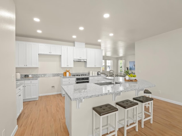 2303 S Bush Ave, Fresno, CA 93727 - kitchen featuring light wood finished floors, white cabinetry, a breakfast bar, a kitchen island with sink, and recessed lighting
