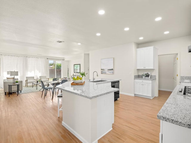 2303 S Bush Ave, Fresno, CA 93727 - kitchen featuring white cabinets, light wood-style floors, an island with sink, recessed lighting, and light stone countertops