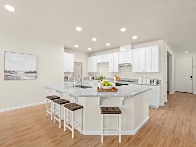 2303 S Bush Ave, Fresno, CA 93727 - kitchen with under cabinet range hood, light wood-style flooring, a kitchen breakfast bar, a large island with sink, and recessed lighting