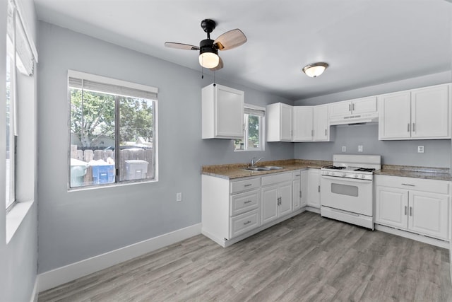4014 E Olive Ave, Fresno, CA 93702 - kitchen featuring white gas stove, under cabinet range hood, healthy amount of natural light, and white cabinetry