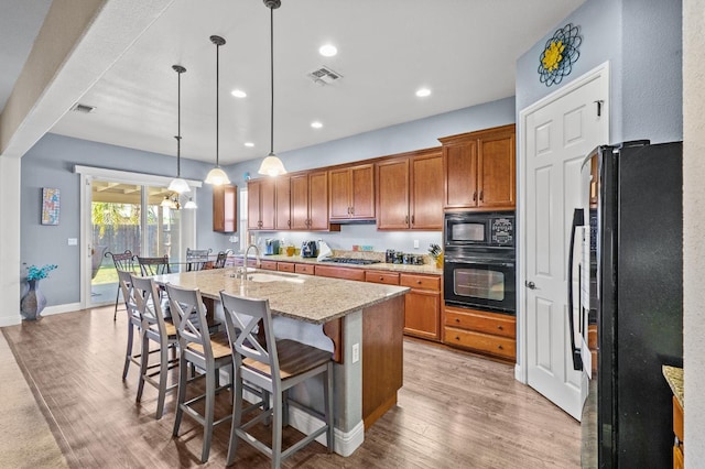 2403 W Robin Ave, Visalia, CA 93291 - kitchen featuring black appliances, brown cabinets, light wood-style floors, a kitchen island with sink, and light stone countertops