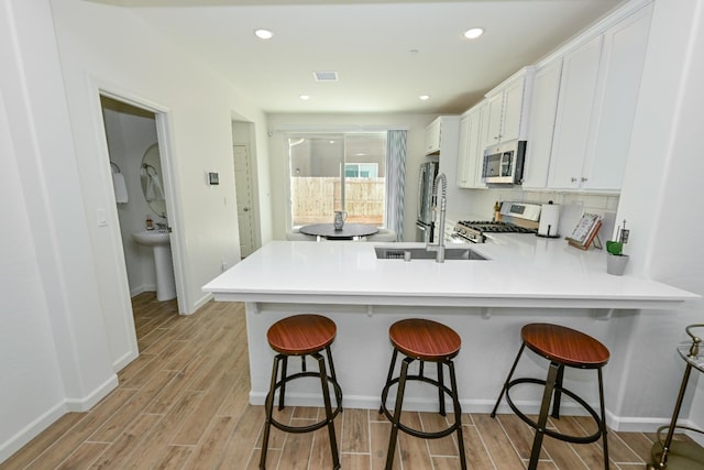 6317 E Malbec Dr, Fresno, CA 93727 - kitchen with appliances with stainless steel finishes, white cabinetry, a kitchen breakfast bar, light wood-style floors, and recessed lighting