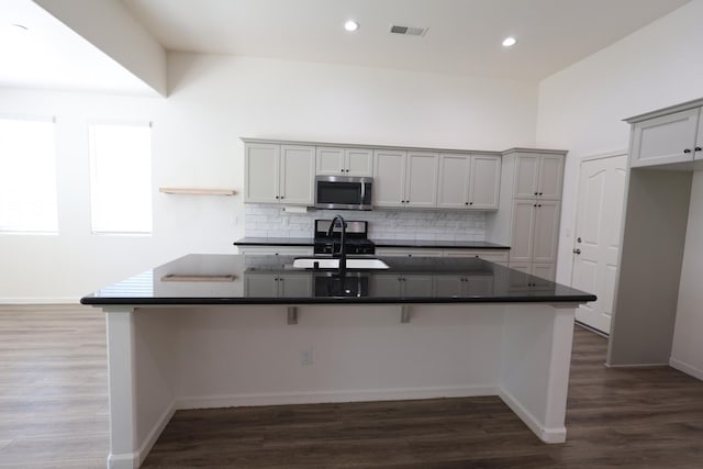 879 Hermosa Ave, Clovis, CA 93619 - kitchen with stainless steel microwave, dark countertops, decorative backsplash, a breakfast bar, and dark wood finished floors