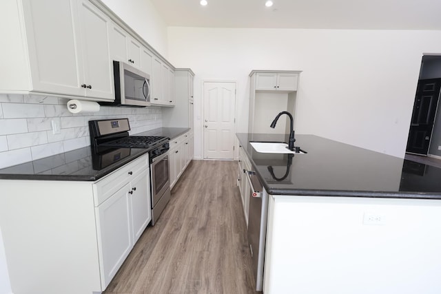 879 Hermosa Ave, Clovis, CA 93619 - kitchen featuring appliances with stainless steel finishes, dark countertops, light wood finished floors, a center island with sink, and decorative backsplash