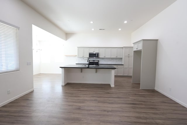 879 Hermosa Ave, Clovis, CA 93619 - kitchen featuring stainless steel microwave, dark countertops, recessed lighting, a kitchen island with sink, and decorative backsplash