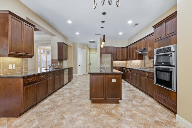 5857 W Modoc, Visalia, CA 93291 - kitchen with appliances with stainless steel finishes, dark stone counters, a kitchen island with sink, decorative backsplash, and recessed lighting