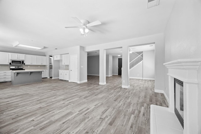 2720 San Jose Ave, Clovis, CA 93611 - unfurnished living room with light wood-style flooring, a ceiling fan, stairway, and a glass covered fireplace