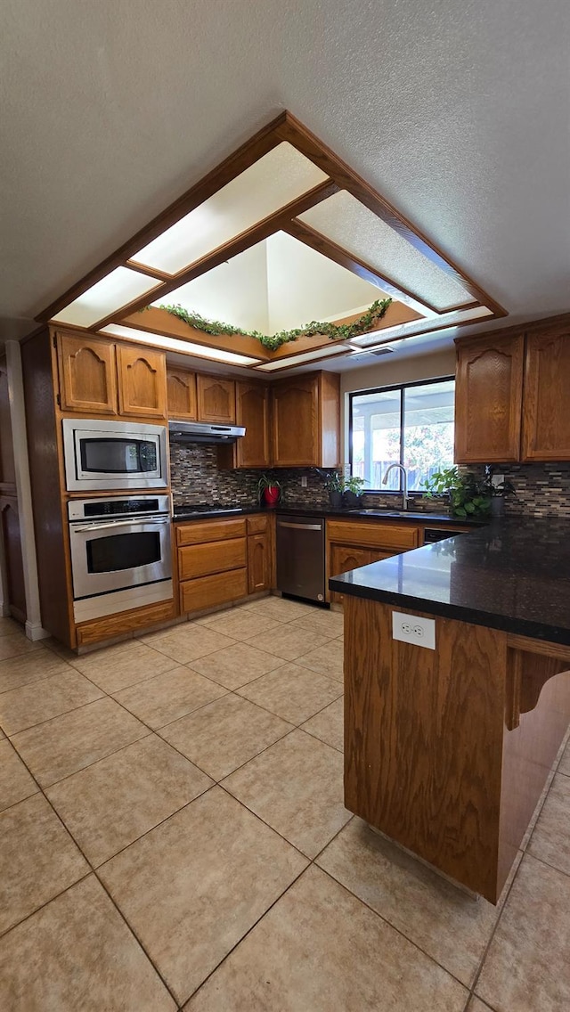 1386 E El Paso Ave, Fresno, CA 93720 - kitchen featuring appliances with stainless steel finishes, a peninsula, tasteful backsplash, brown cabinetry, and a textured ceiling
