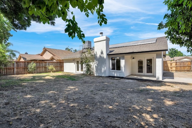 1033 Cypress Ct, Madera, CA 93637 - back of house featuring french doors, roof mounted solar panels, a fenced backyard, stucco siding, and a chimney