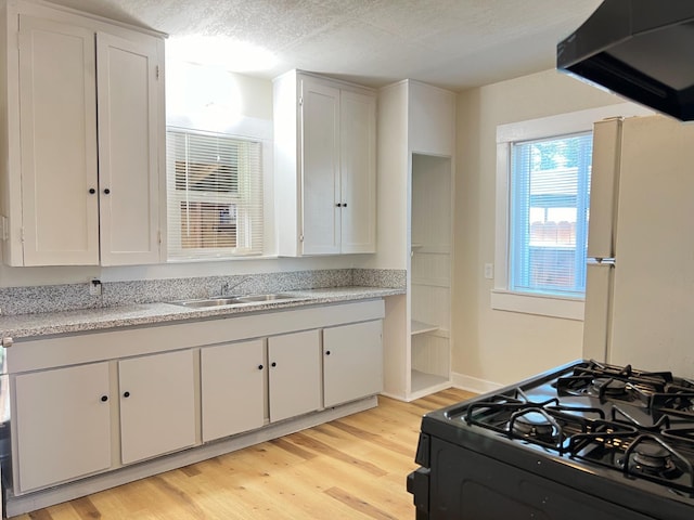 2405 E White Ave, Fresno, CA 93701 - kitchen with black range with gas cooktop, freestanding refrigerator, range hood, light wood-type flooring, and white cabinetry