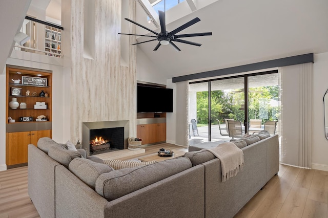 2734 W Bluff Ave, Fresno, CA 93711 - living area with high vaulted ceiling, a lit fireplace, light wood-style flooring, a ceiling fan, and a skylight