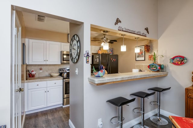 5090 N College Ave Unit 103, Fresno, CA 93704 - kitchen with stainless steel appliances, a breakfast bar area, white cabinets, dark wood finished floors, and decorative backsplash