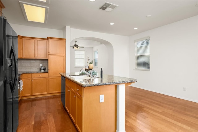 1935 N Glen Alva Ln, Clovis, CA 93619 - kitchen featuring wood finished floors, a kitchen island with sink, black appliances, dark stone counters, and arched walkways