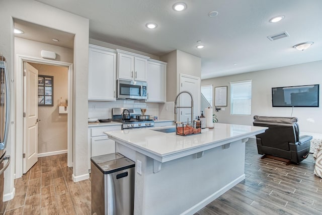 212 Arbor Dr S, Madera, CA 93636 - kitchen featuring stainless steel appliances, light wood-style floors, a center island with sink, white cabinetry, and light countertops