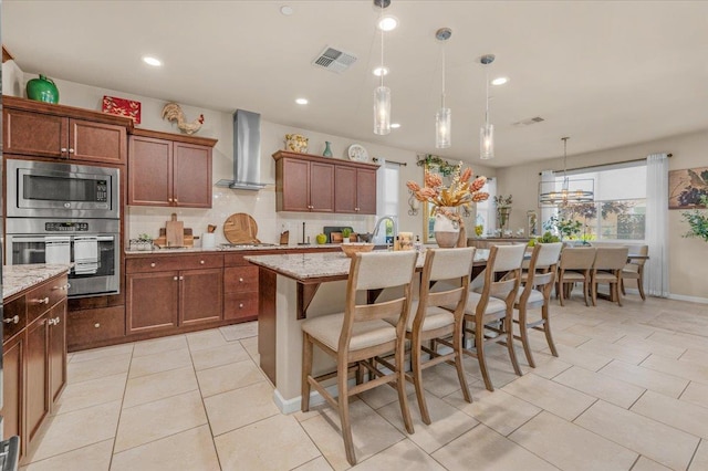 3982 Flint Ave, Clovis, CA 93619 - kitchen with stainless steel appliances, wall chimney range hood, decorative backsplash, light tile patterned flooring, and a kitchen island with sink