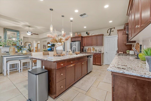 3982 Flint Ave, Clovis, CA 93619 - kitchen with stainless steel appliances, a ceiling fan, a center island with sink, decorative light fixtures, and light stone countertops