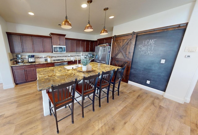 4367 Salem Ln, Clovis, CA 93619 - kitchen with appliances with stainless steel finishes, a kitchen breakfast bar, a barn door, light wood-type flooring, and a kitchen island with sink