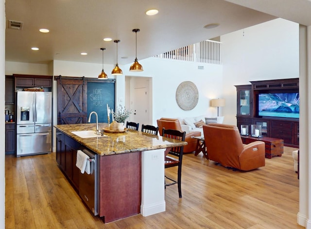 4367 Salem Ln, Clovis, CA 93619 - kitchen featuring appliances with stainless steel finishes, a breakfast bar area, a barn door, light wood finished floors, and light stone countertops
