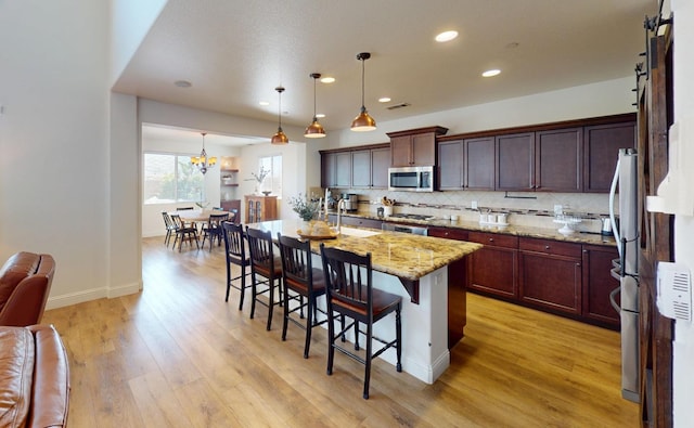 4367 Salem Ln, Clovis, CA 93619 - kitchen featuring stainless steel appliances, light wood finished floors, a breakfast bar, tasteful backsplash, and light stone counters