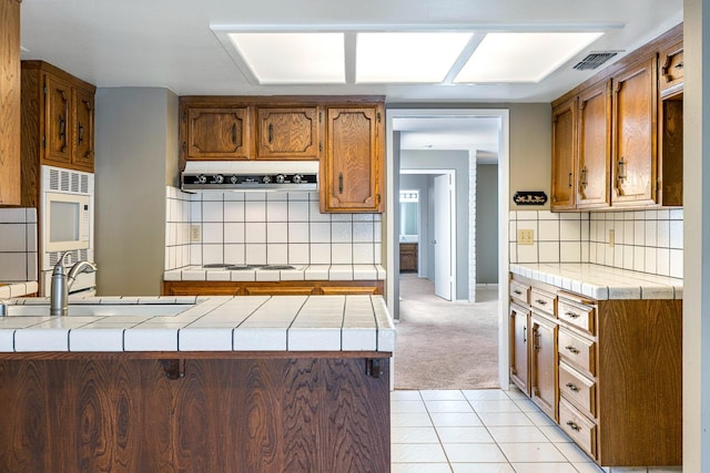 2076 W Calimyrna Ave Unit 102, Fresno, CA 93711 - kitchen with backsplash, tile counters, brown cabinetry, a peninsula, and white appliances
