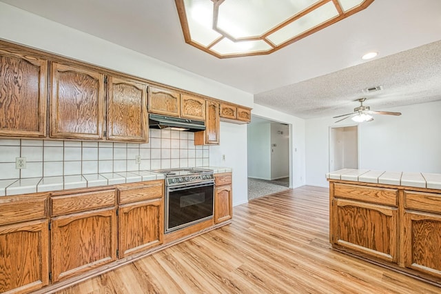 11016 E S Ave, Selma, CA 93662 - kitchen with stainless steel electric range oven, tile countertops, under cabinet range hood, decorative backsplash, and light wood-style floors