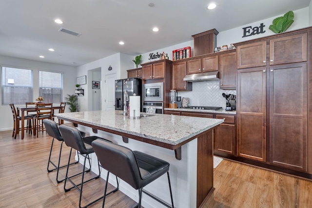 915 Winchell Way W, Madera, CA 93636 - kitchen featuring appliances with stainless steel finishes, under cabinet range hood, a breakfast bar area, a center island, and light wood-type flooring
